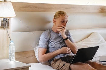Yawning freelancer working online on hotel bed