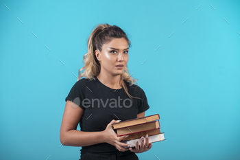 Female student holding a heavy stock of books