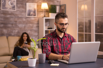 Bearded freelancer working on laptop in living room stock photo NULLED