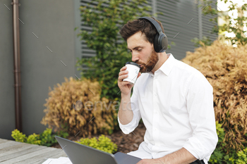 Freelancer in headphones enjoying coffee and using laptop stock photo NULLED