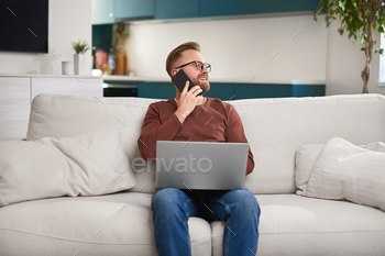 Male freelancer with laptop speaking on smartphone stock photo NULLED