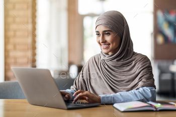 Positive muslim girl freelancer working at cafe stock photo NULLED