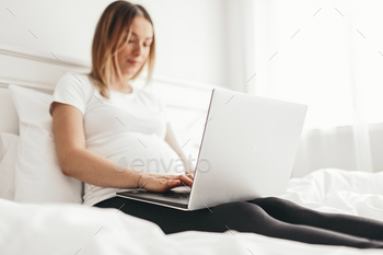 Pregnant freelancer using laptop on bed stock photo NULLED