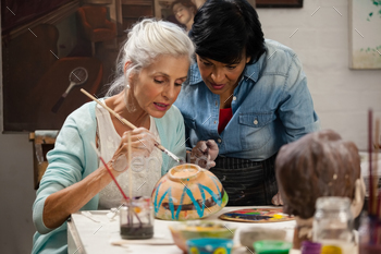 Woman assisting senior woman in painting bowl at drawing class