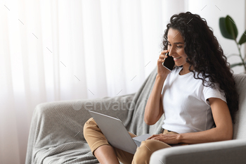 Woman freelancer talking on phone and using laptop stock photo NULLED